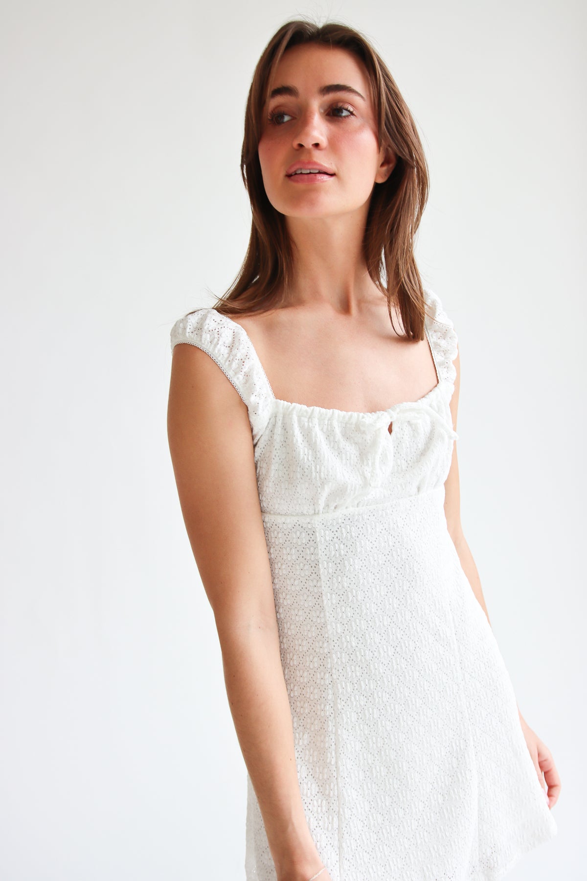 Woman wearing white eyelet fit and flare mini dress with square neckline and cap sleeves against white background