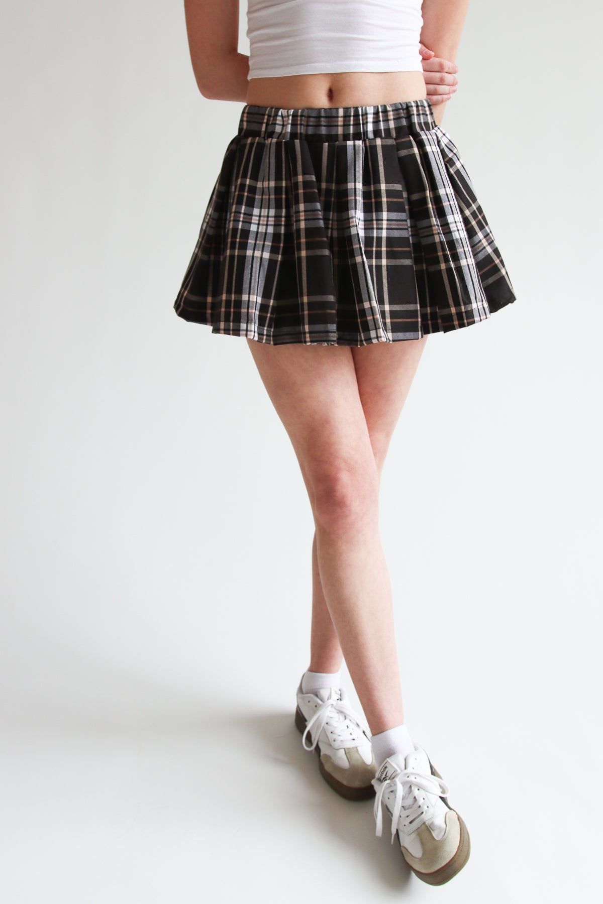 Woman wearing a black pleated plaid mini skort with elastic waistband paired with white sneakers and socks