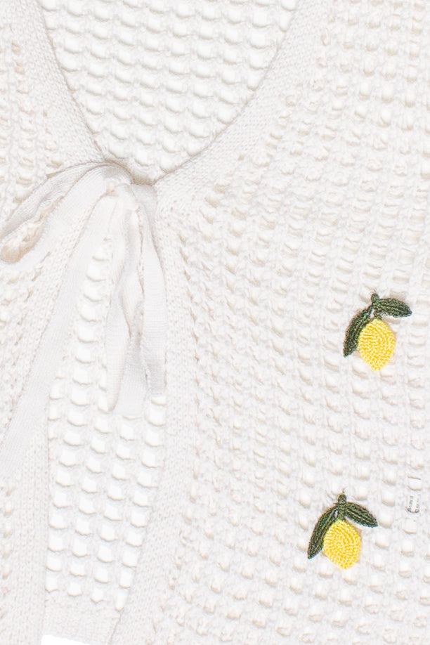 Close-up of white mesh stitch tie front cardigan with small embroidered yellow lemons on textured fabric
