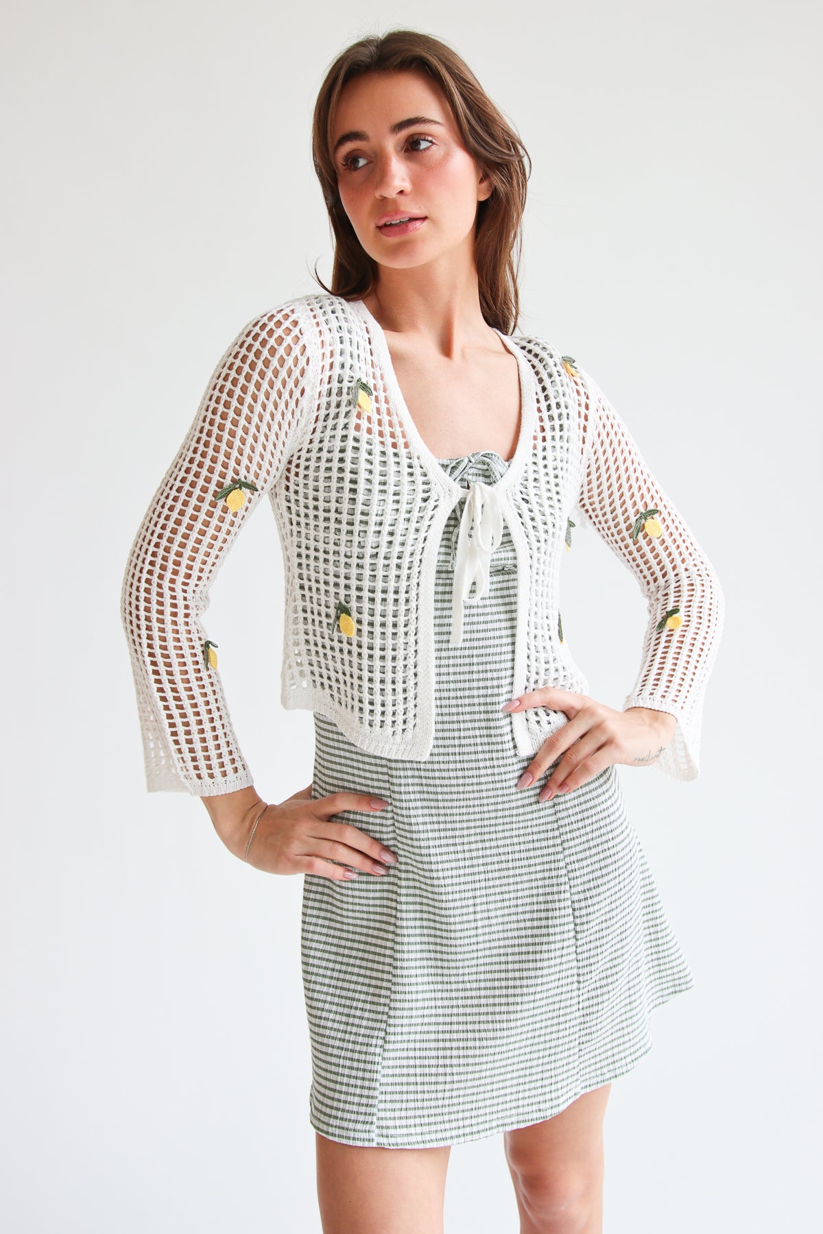 Woman wearing a white mesh stitch tie front cardigan with small fruit details over a green checkered dress
