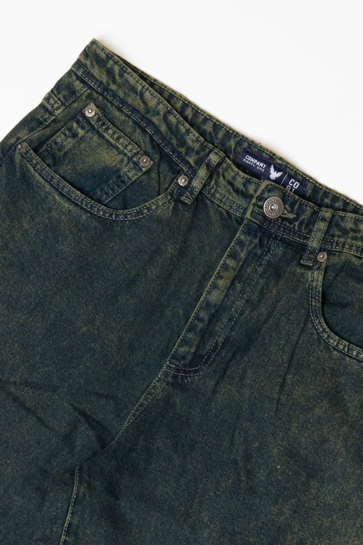 Close-up of dark green acid-washed denim jeans with silver button and Company Eighty One brand tag