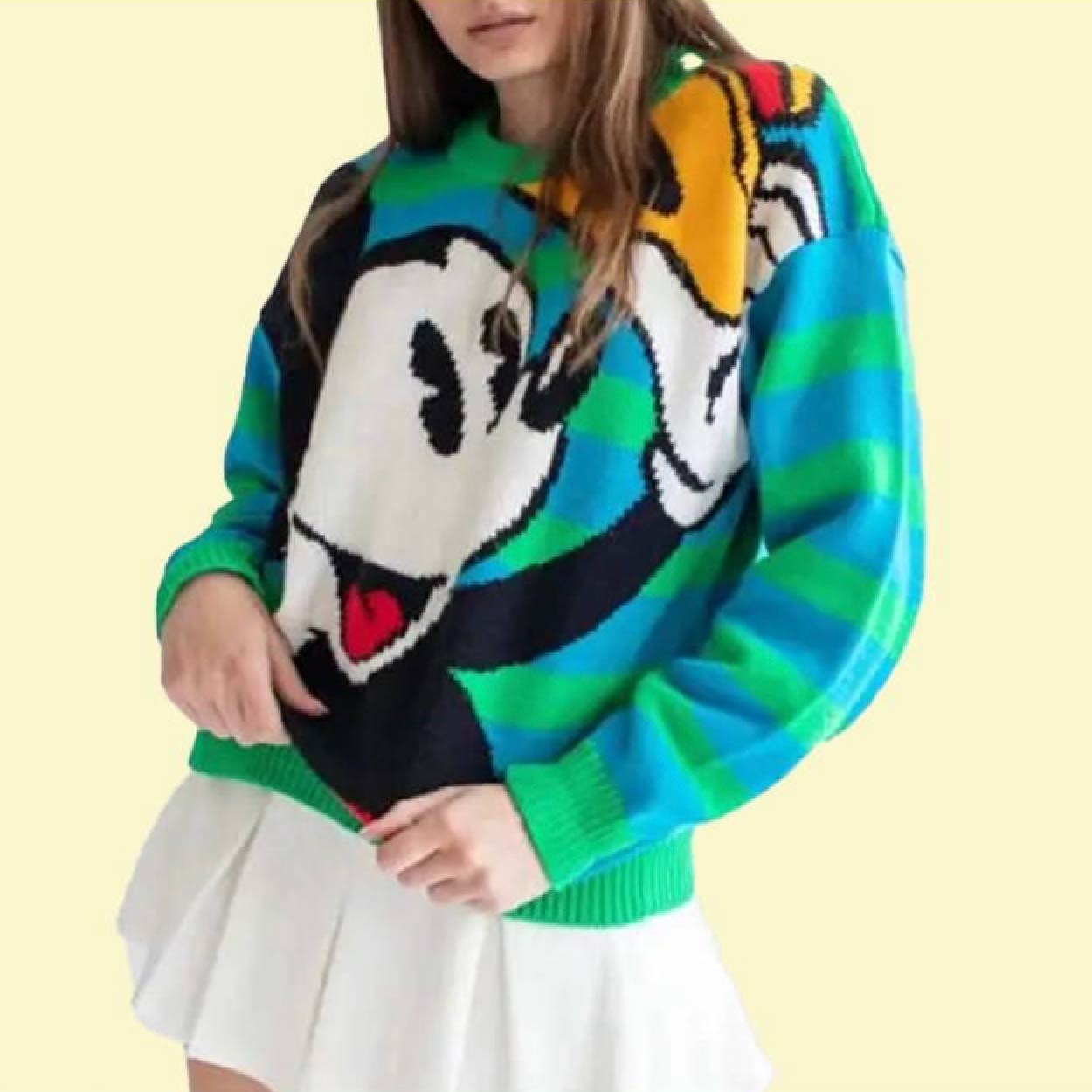 Woman wearing a bright green Mickey Mouse 90's knit sweater over a white pleated skirt