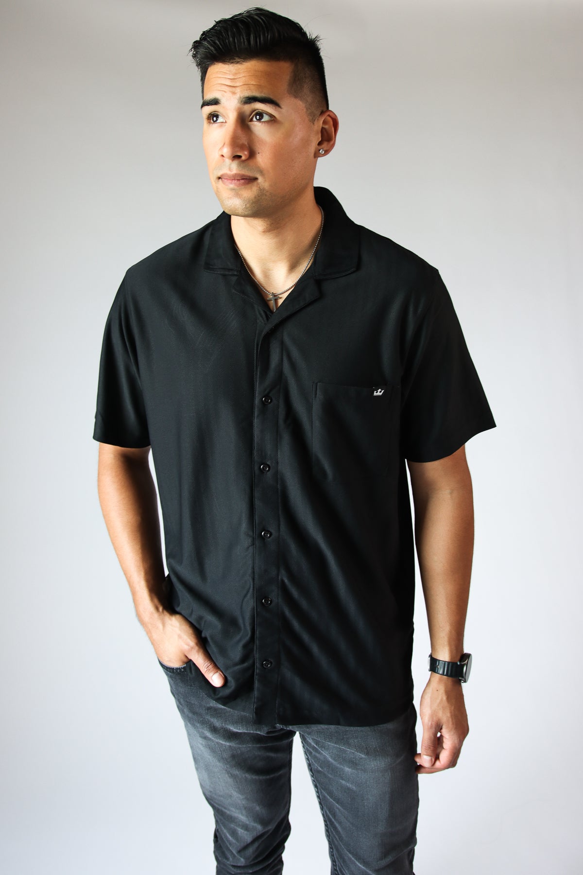 Man wearing black Micro Herringbone Knit Button Up Shirt with short sleeves and pocket on chest standing against white background