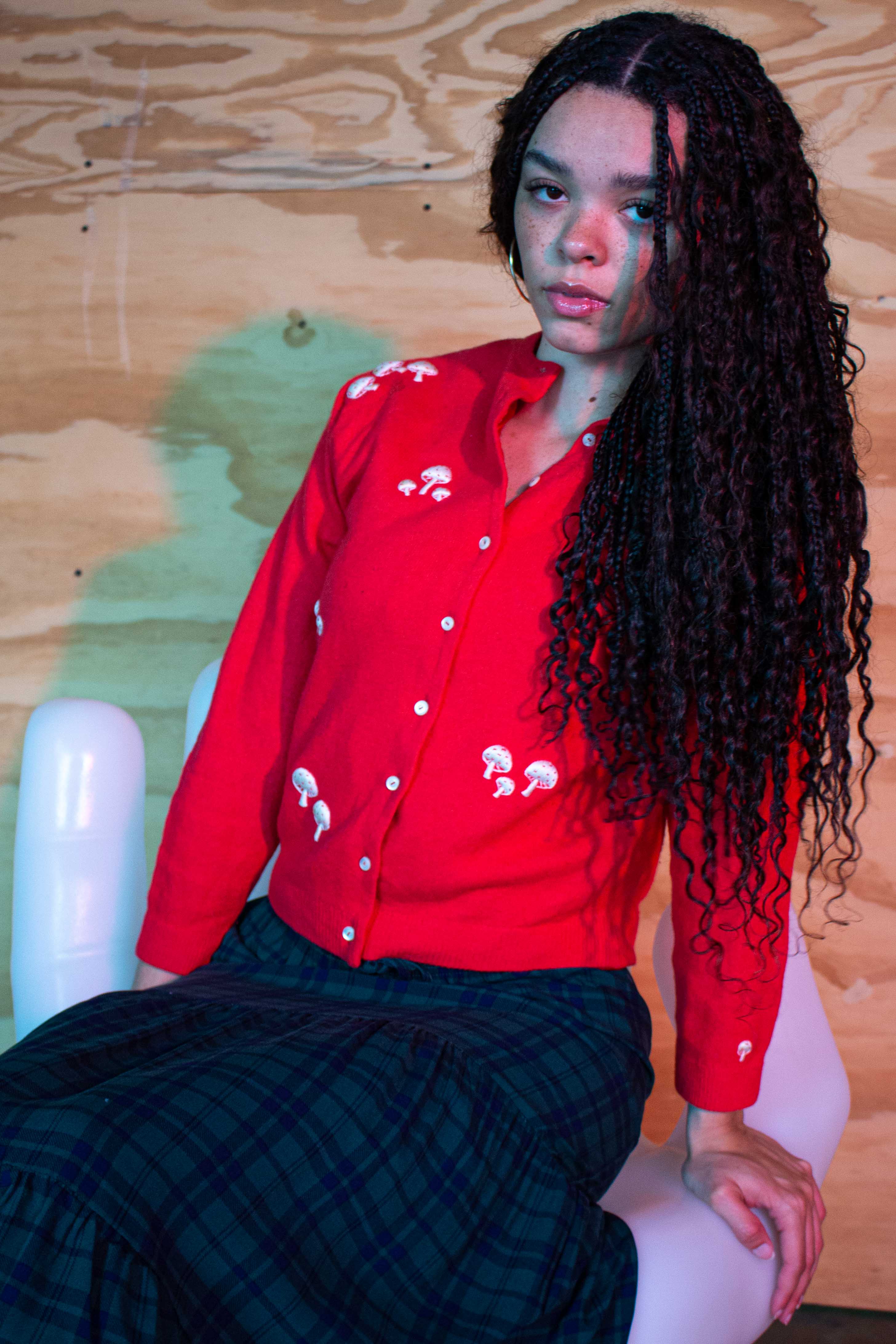 Woman wearing vintage red hand embroidered sweater with white mushroom designs sitting on white chair