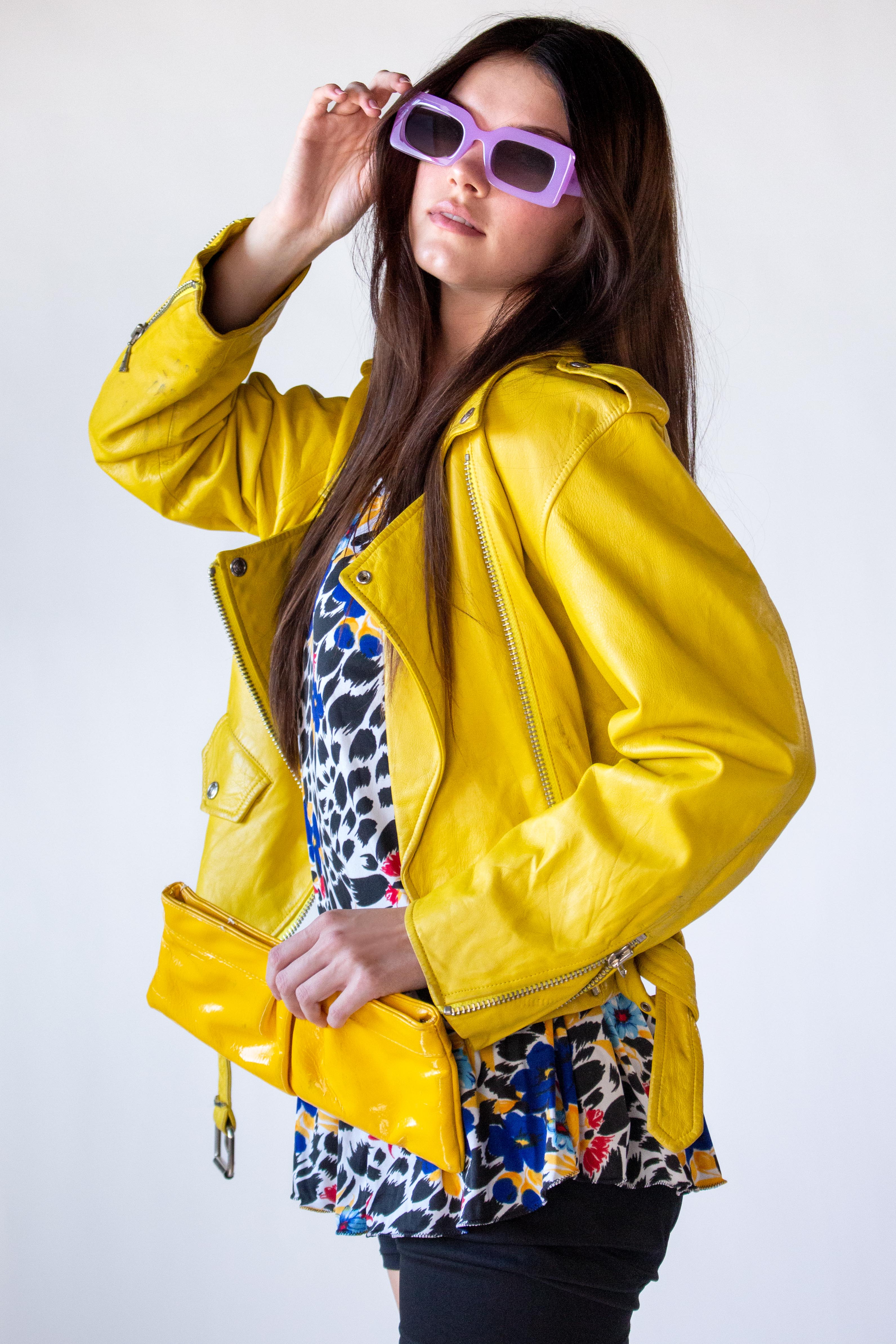 Woman wearing a yellow leather jacket and colorful dress against a white background