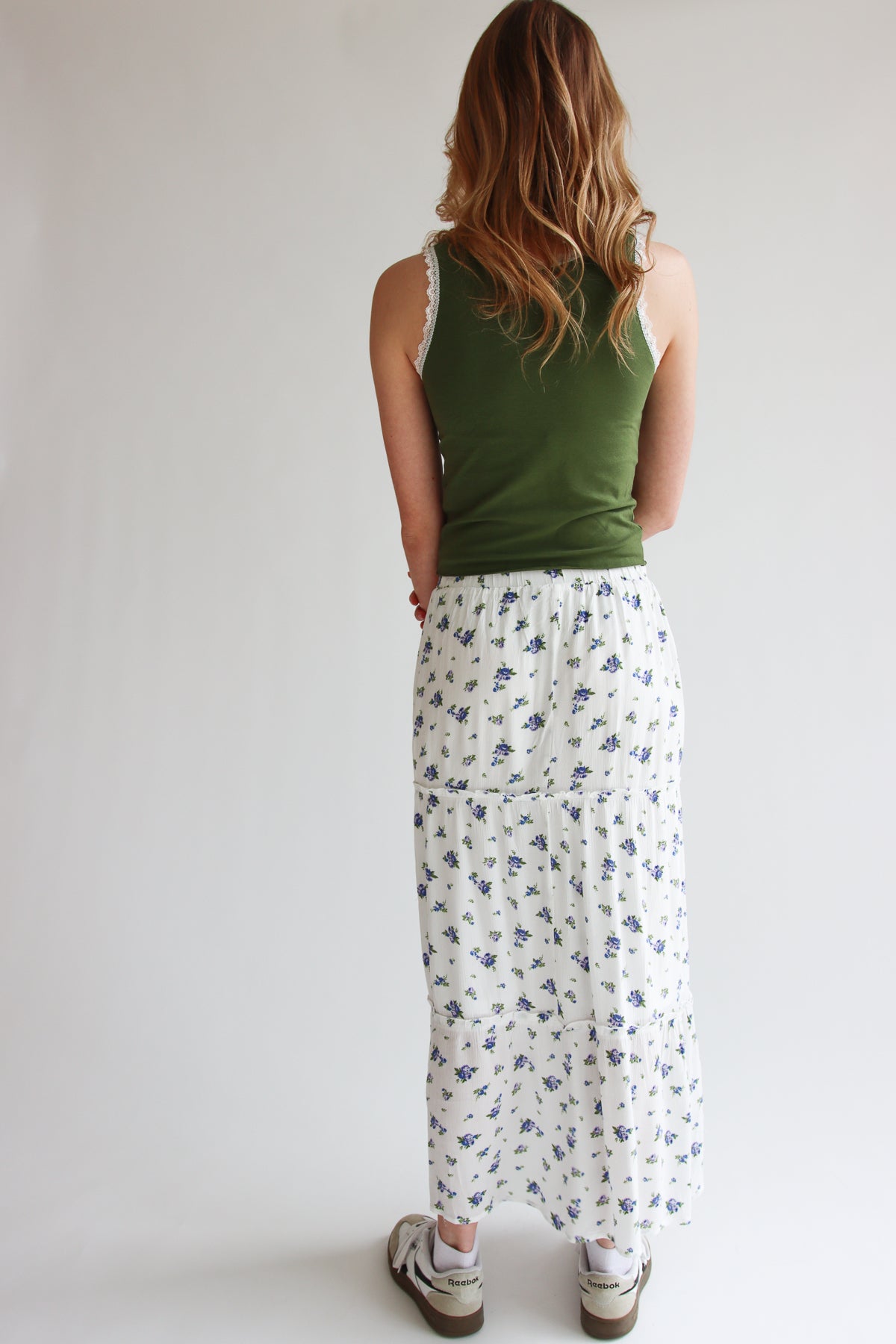 Woman wearing a rose pattern tiered maxi skirt with elastic waistband and white background with small floral print from back view