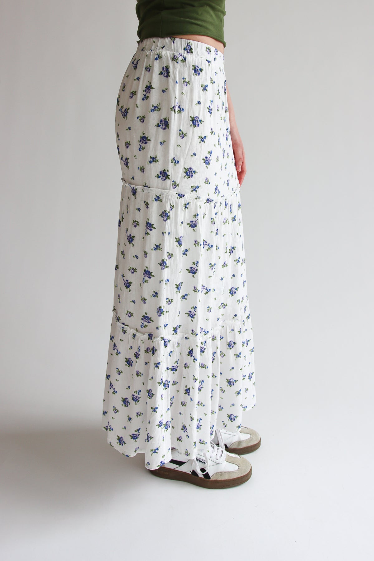 Side view of white tiered maxi skirt with blue rose pattern and elastic waistband worn with sneakers