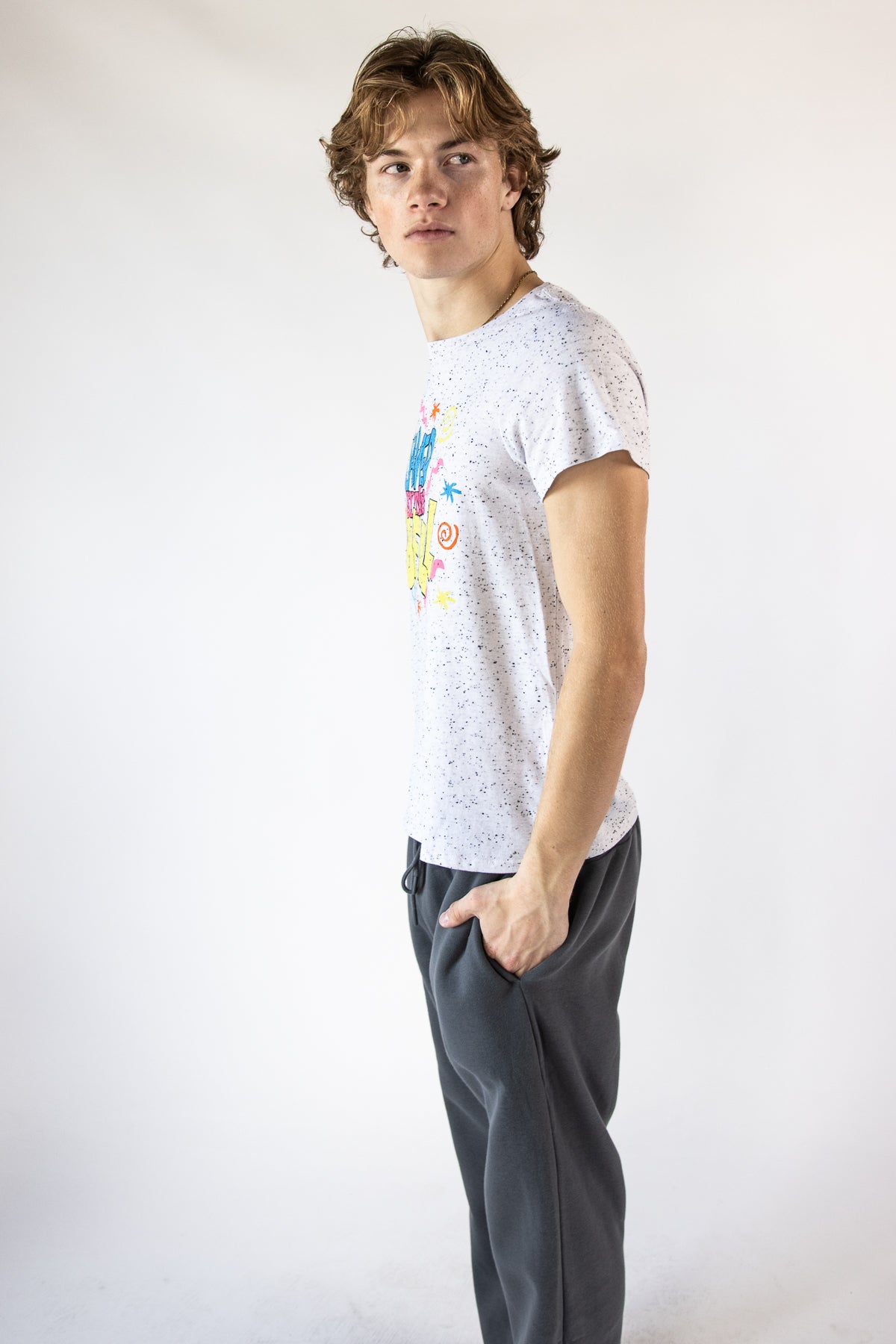 Man wearing a white speckled graphic t-shirt and charcoal sweatpants shown in side profile