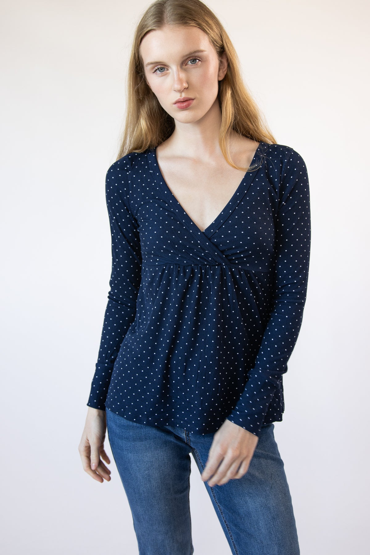 Woman wearing a navy blue polka dot long-sleeve top with a V-neck and empire waist