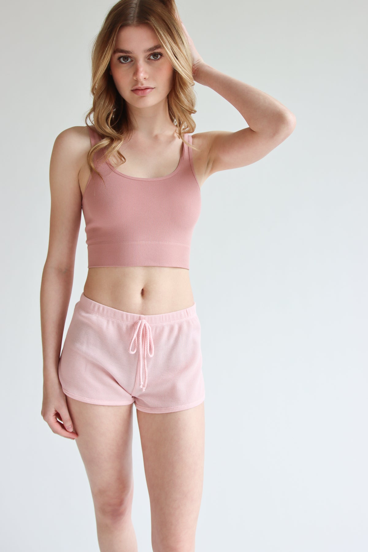 Woman wearing light pink Thermal Dolphin Shorts and matching cropped tank top standing against white background