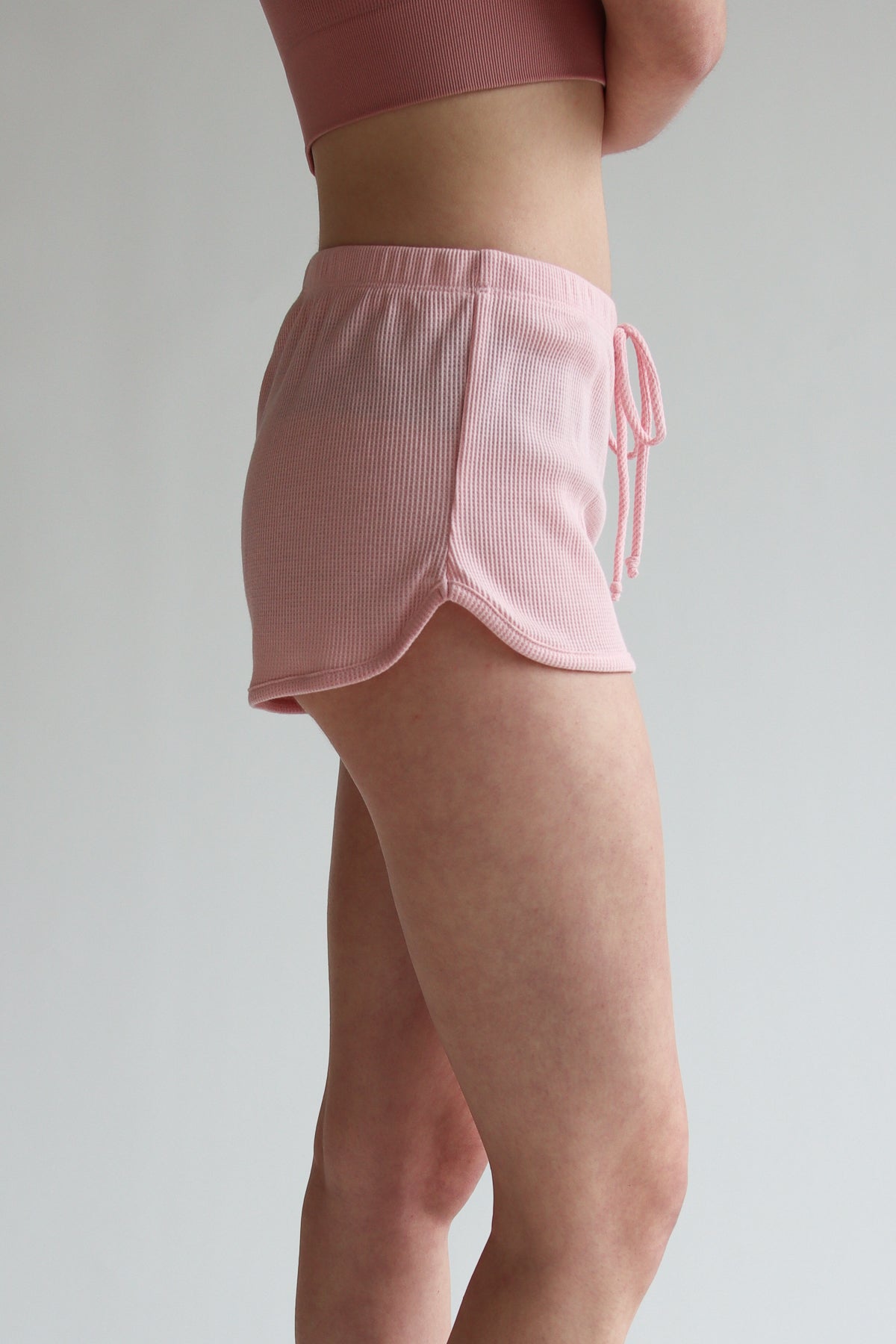 Side view of a model wearing pink Thermal Dolphin Shorts with a drawstring waist on a plain background
