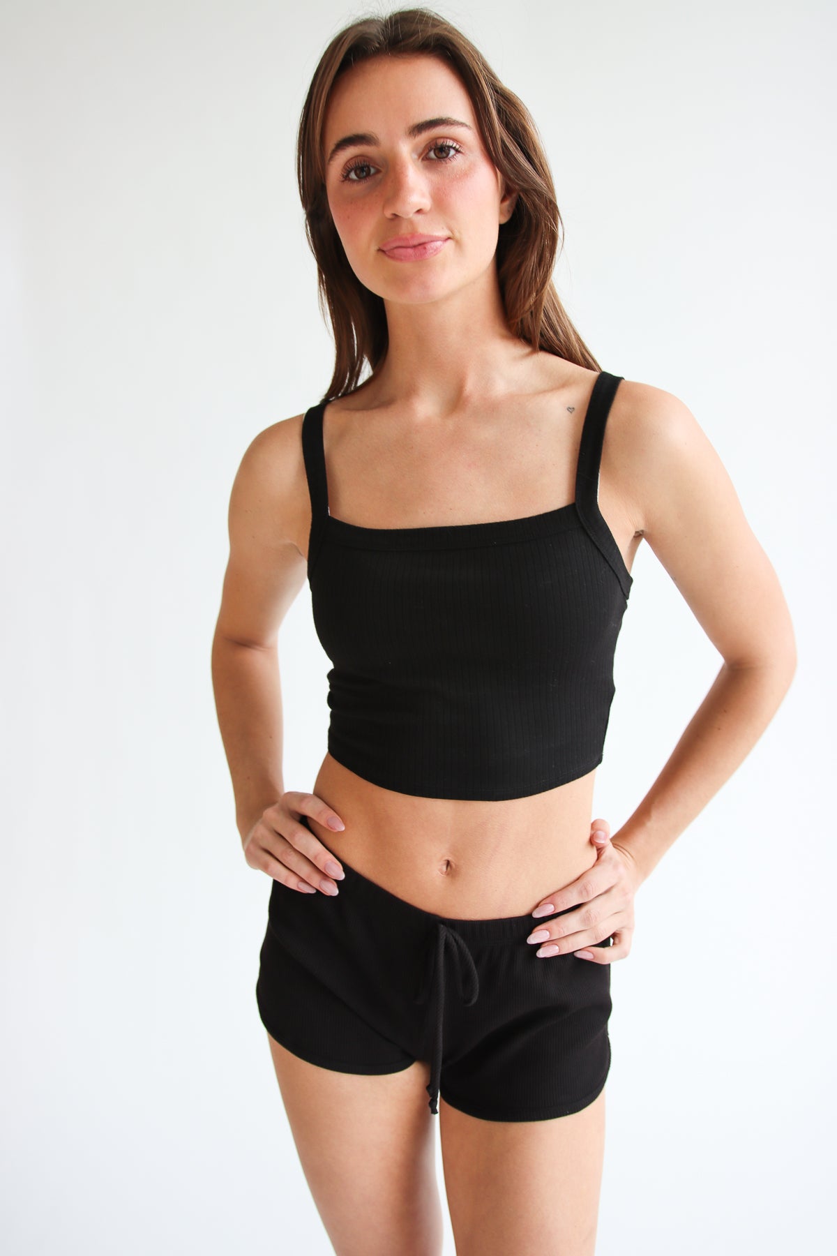 Woman wearing black Thermal Dolphin Shorts and black crop top posing against white background