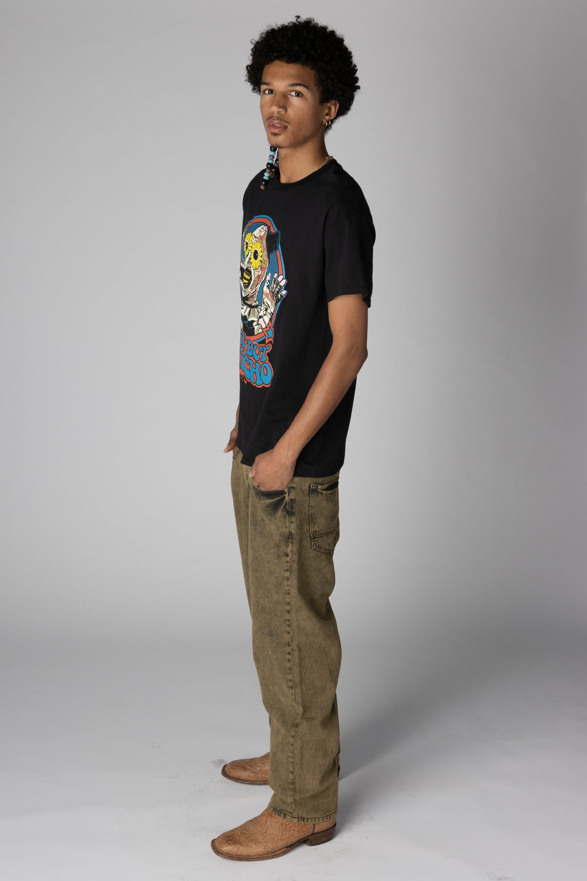 Man in profile wearing a black graphic t-shirt, washed olive wide-leg jeans, and brown boots