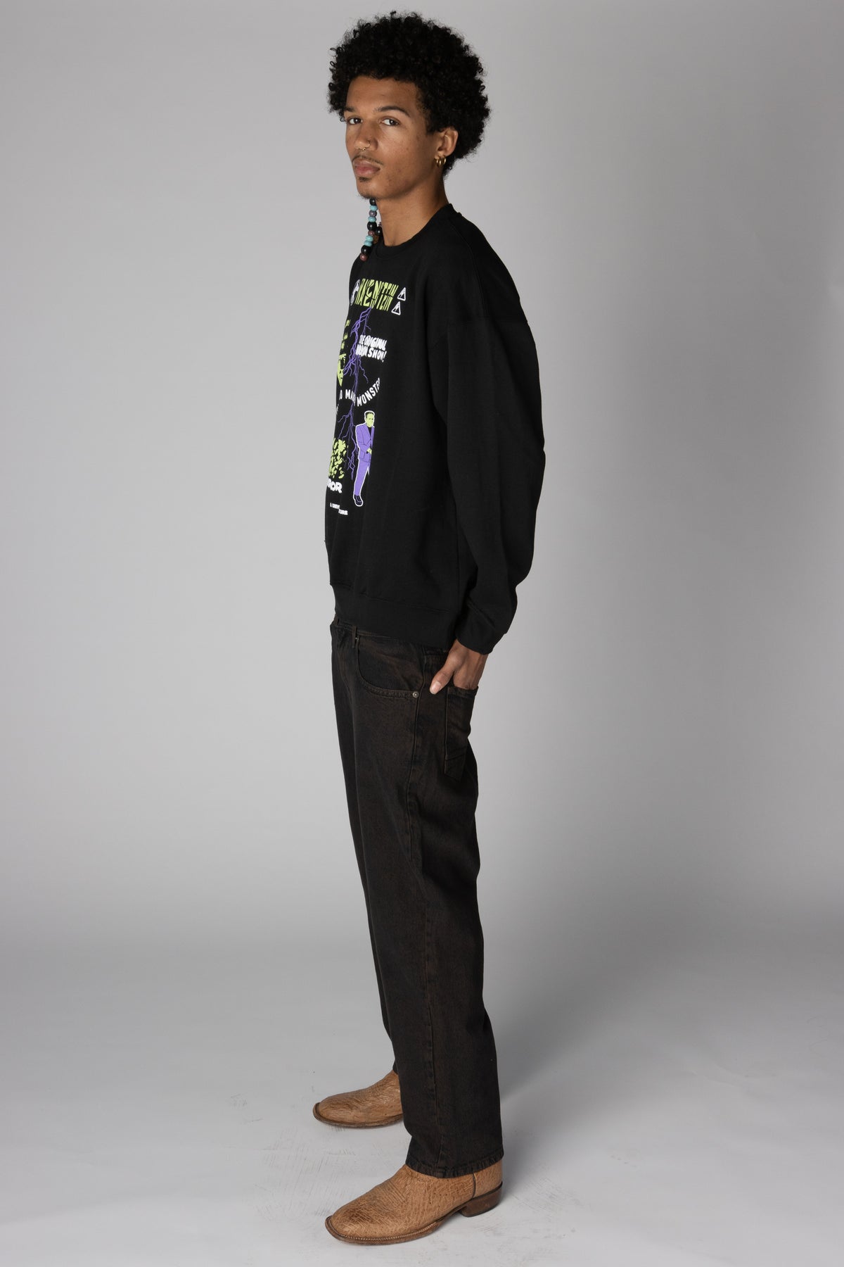 Side view of a man wearing a black graphic sweatshirt with Frankenstein print and black jeans