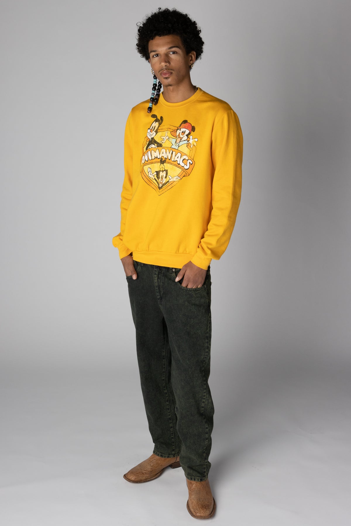 Man wearing a yellow Animaniacs graphic sweatshirt with dark grey jeans