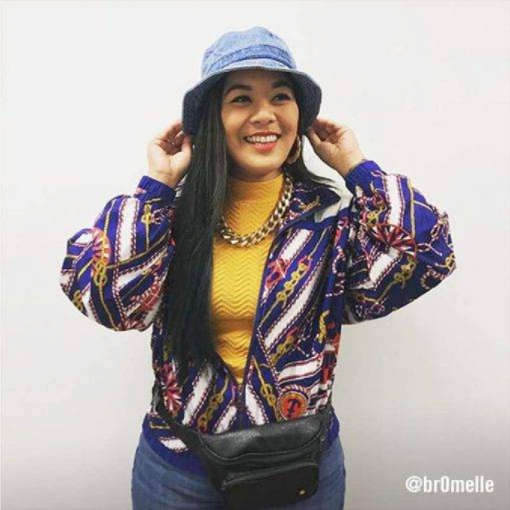 @br0melle wearing the classic hip-hop inspired 90's look. A loud patterned 90's windbreaker, a bucket hat, a fanny pack, and chunky gold jewlery.