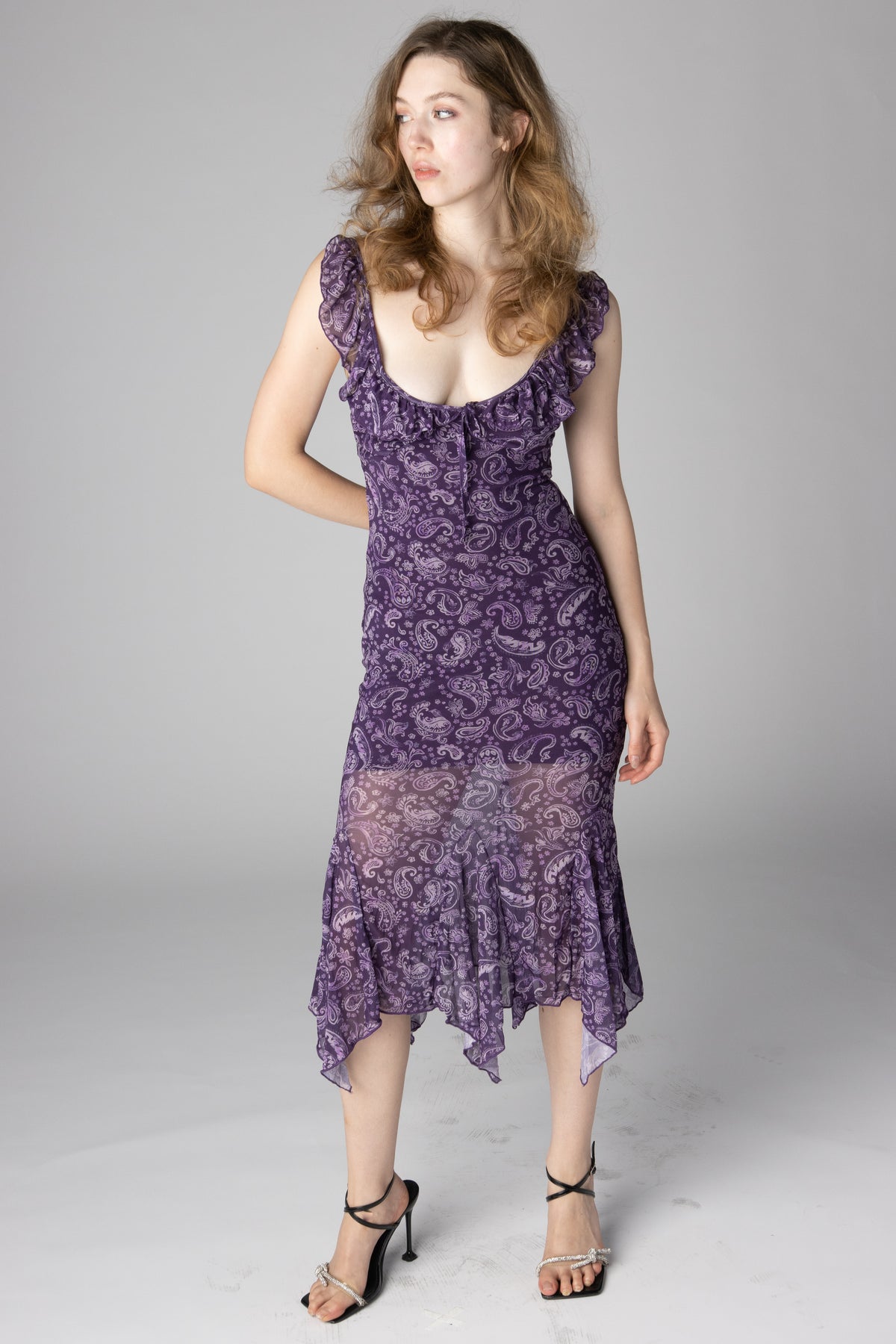Woman modeling purple paisley print midi dress with ruffled scoop neck and handkerchief hem
