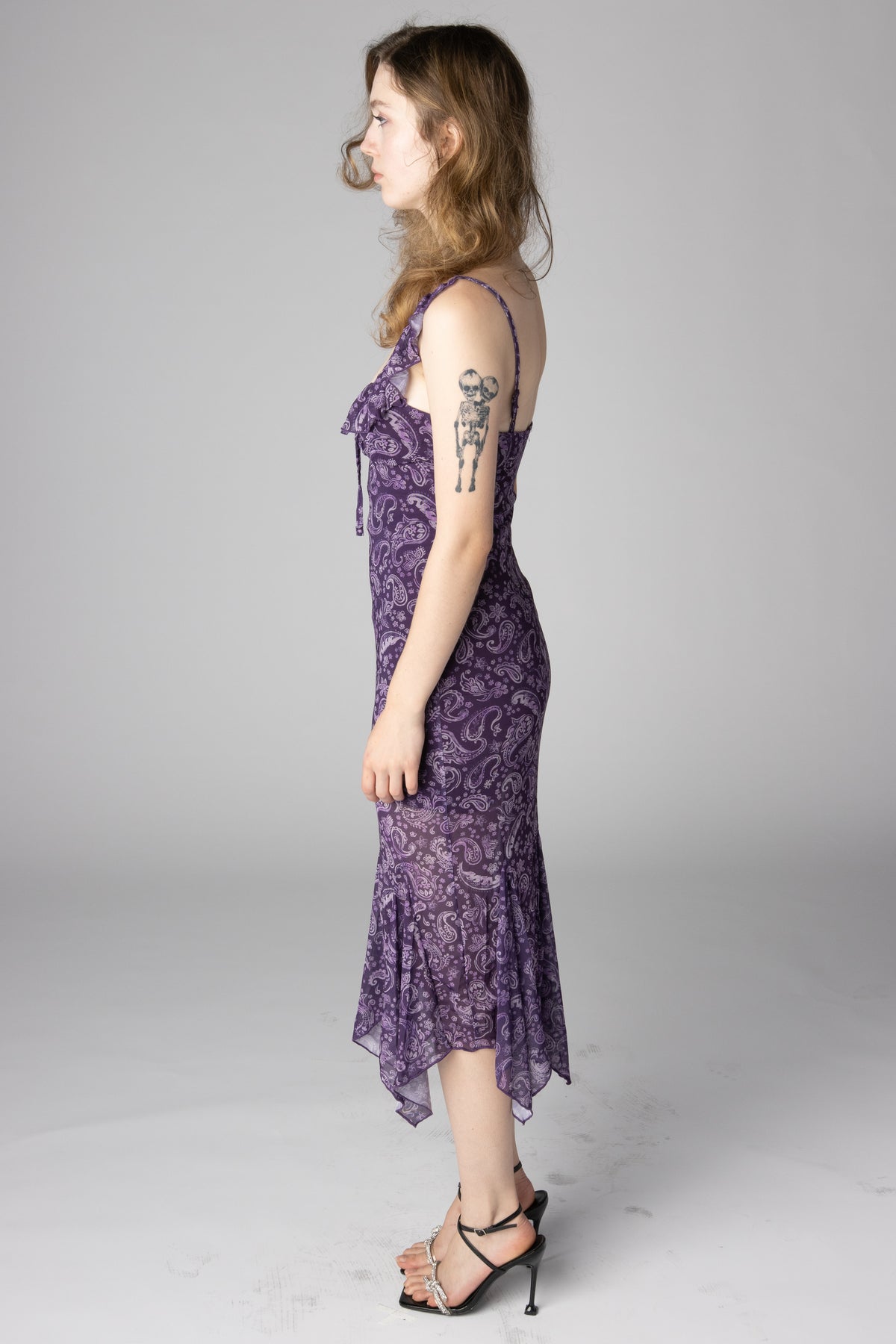 Side profile of a woman wearing a purple paisley print midi dress and black strappy high heels