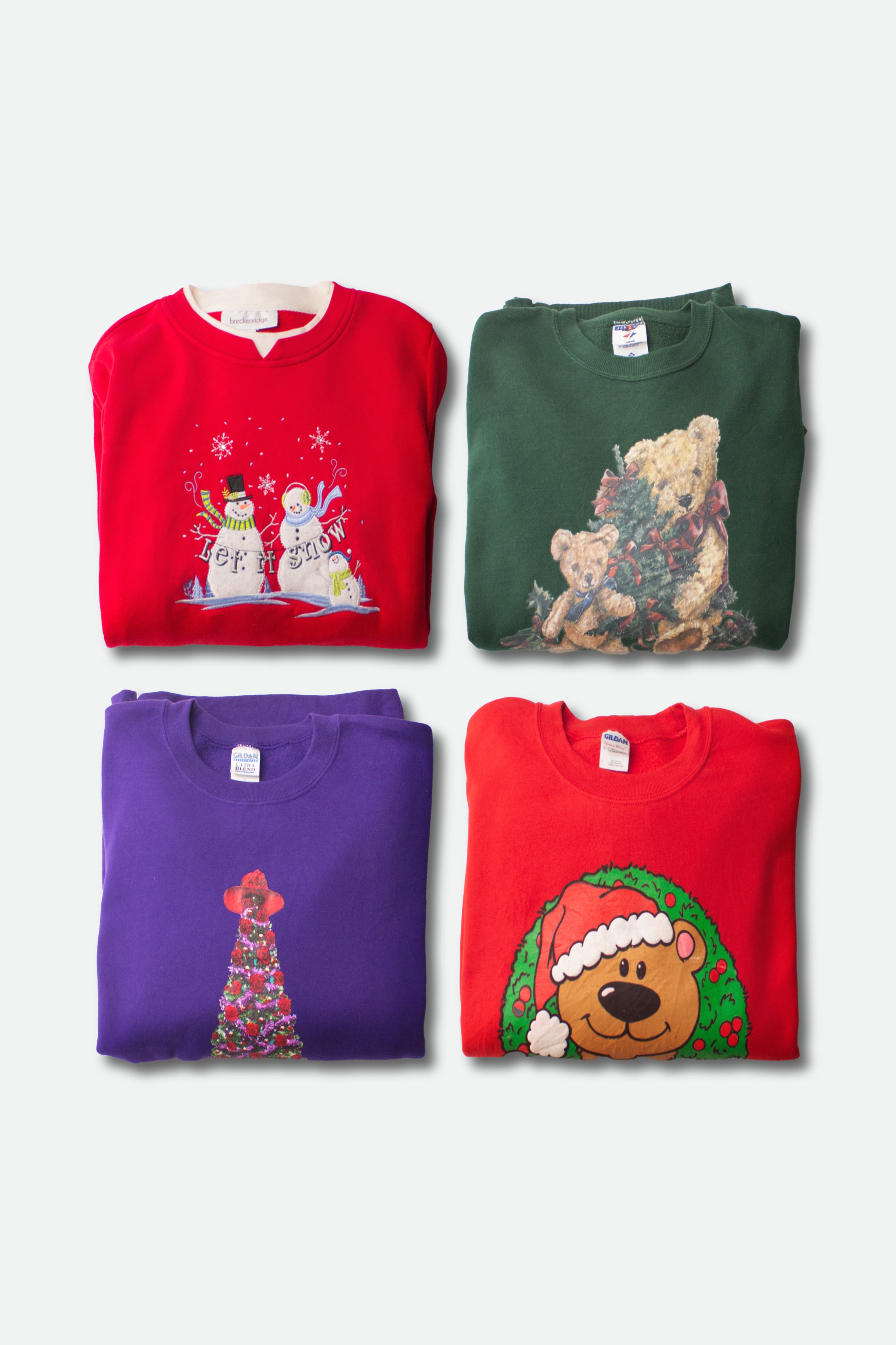 Four folded vintage ugly Christmas sweatshirts in red, green, purple, and red with festive holiday designs.