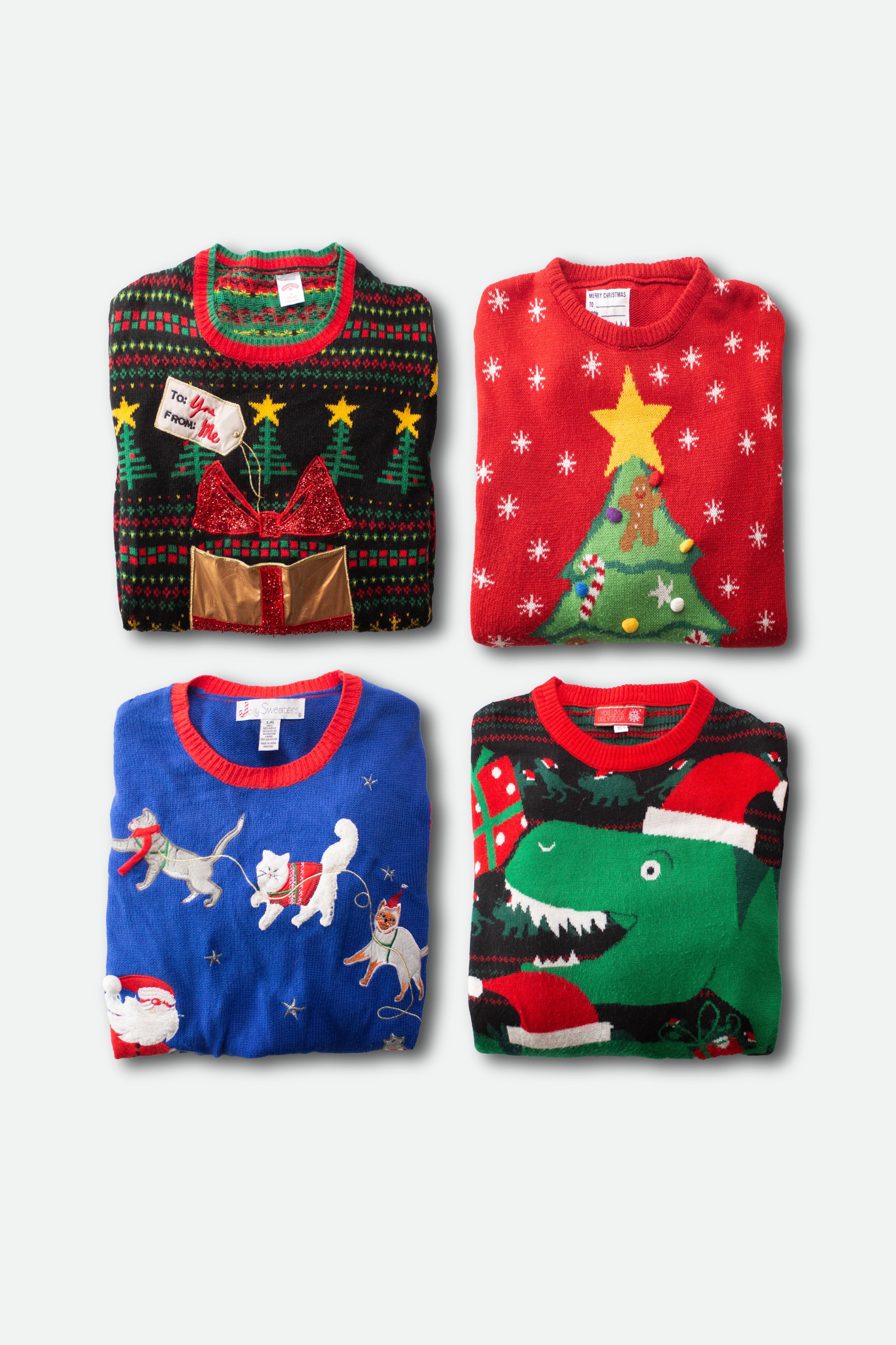 Four folded colorful modern ugly Christmas sweaters with festive holiday designs on a white background