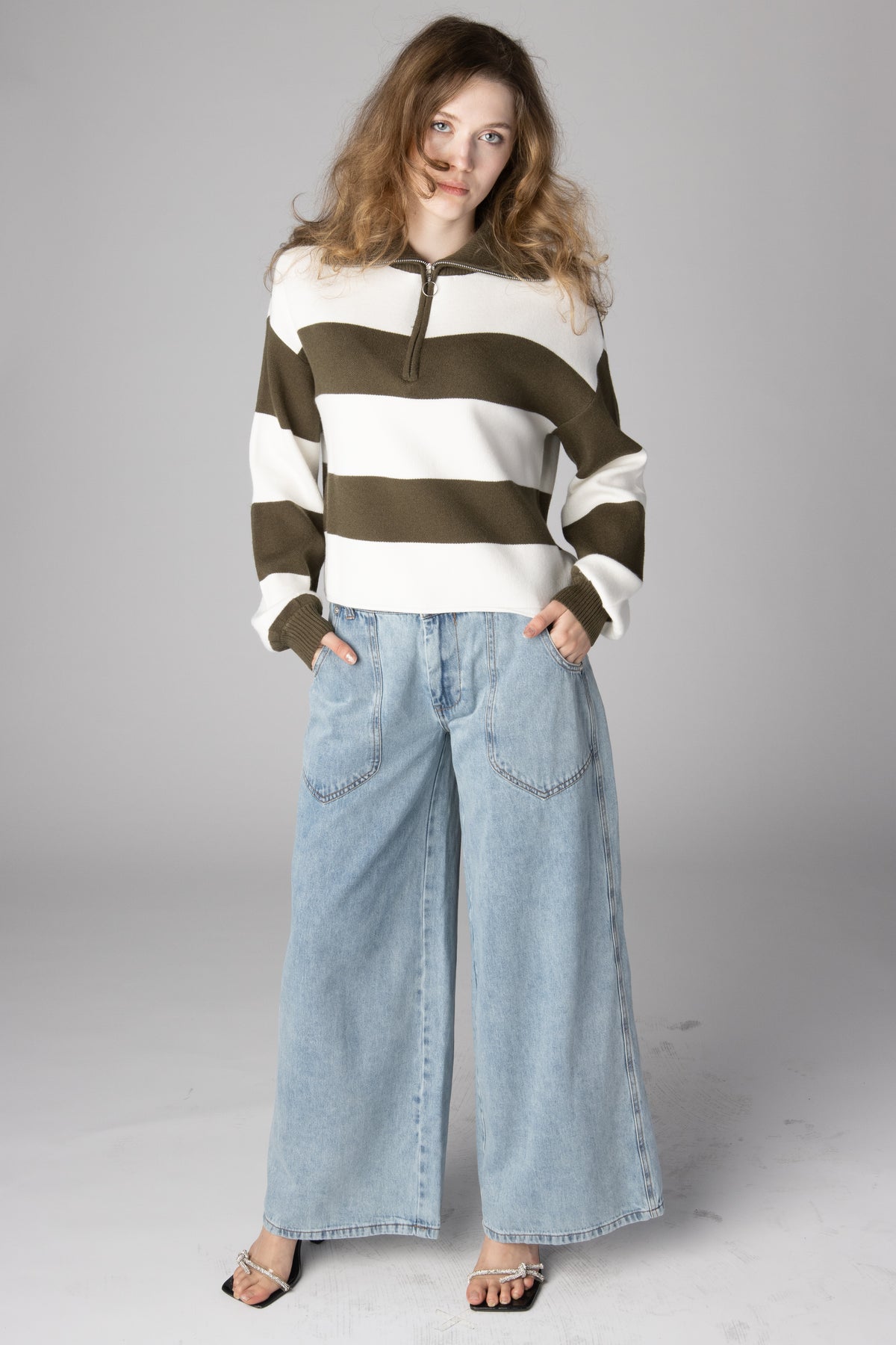 Woman wearing an olive green and white striped half-zip sweater with light wash wide-leg jeans