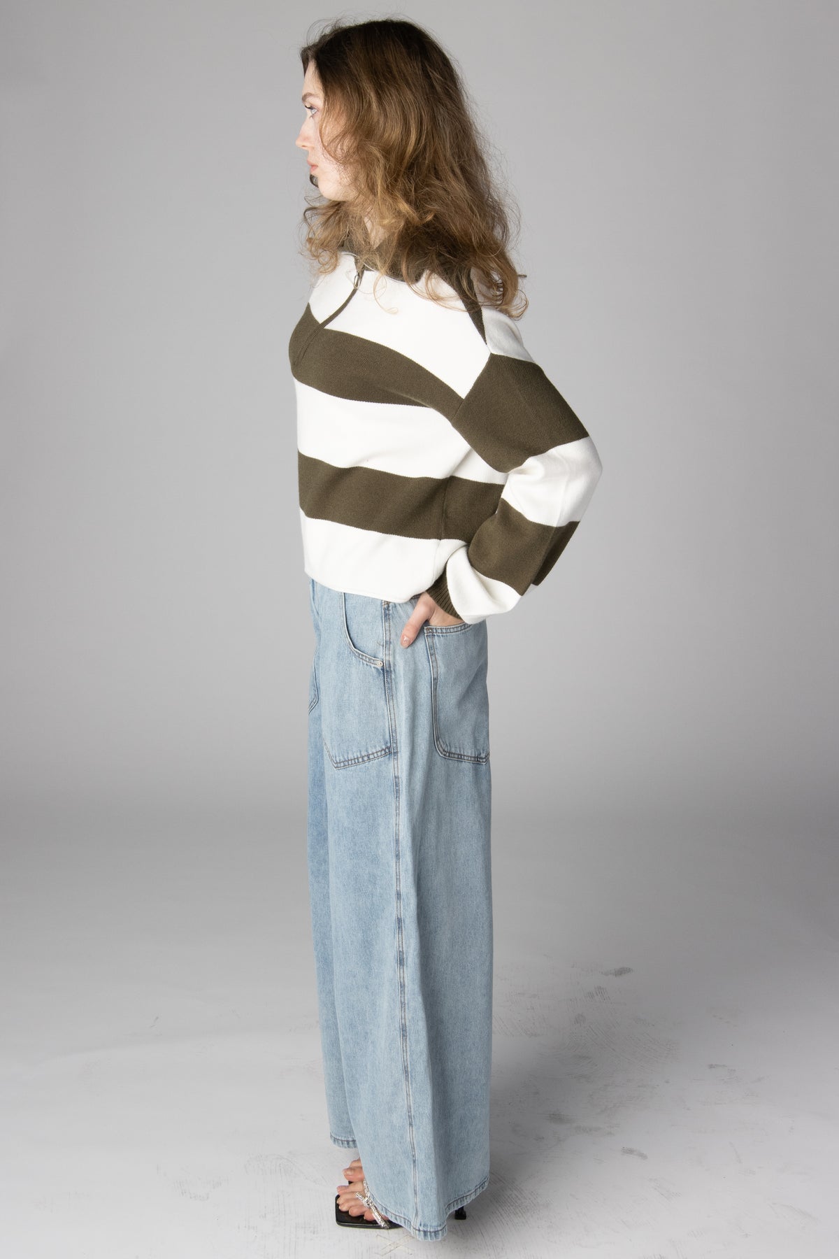 Woman wearing an olive green and white striped knit sweater with light-wash wide-leg jeans