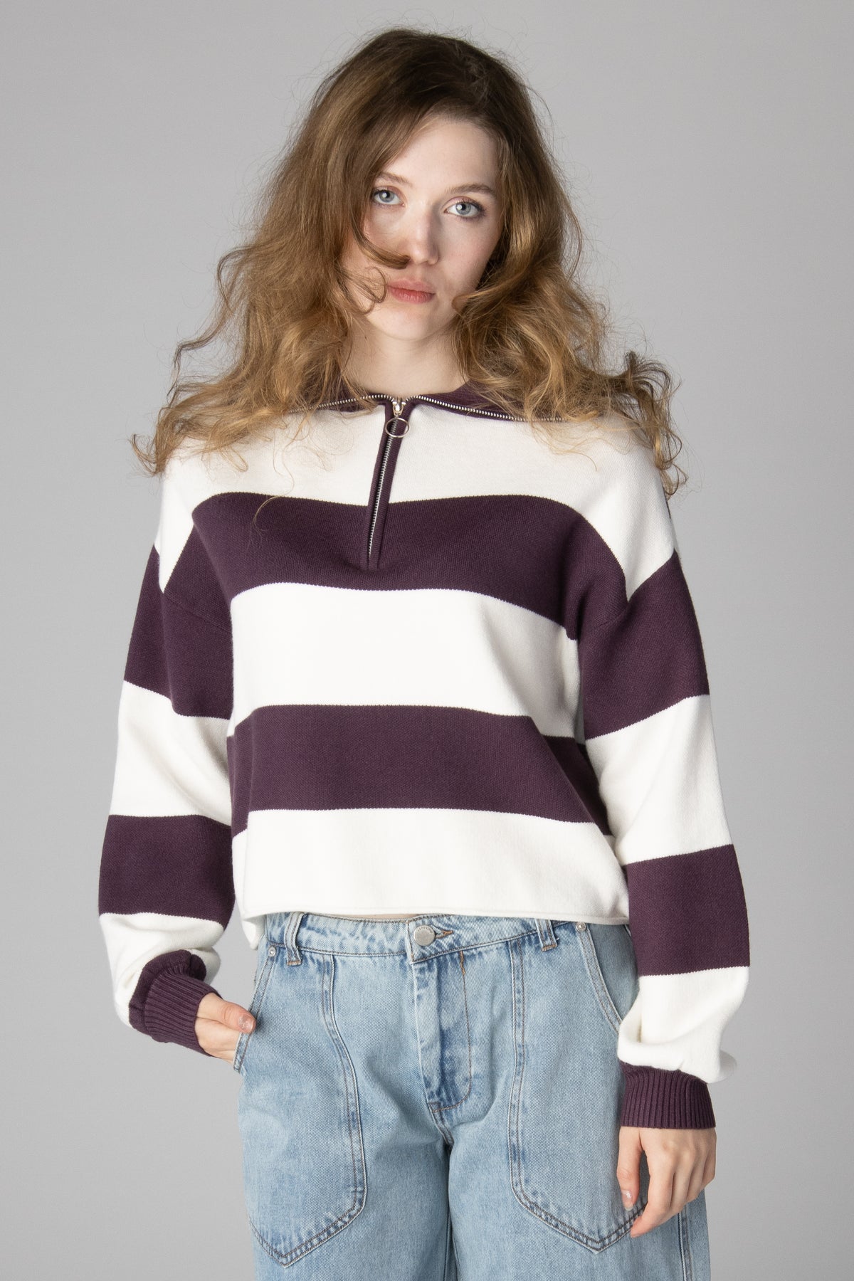 Woman wearing a cropped white and dark purple striped half-zip knit sweater with jeans