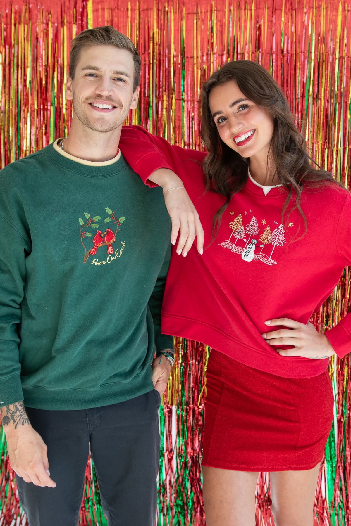 Man and woman smiling in festive vintage-inspired Christmas sweatshirts against red and gold backdrop