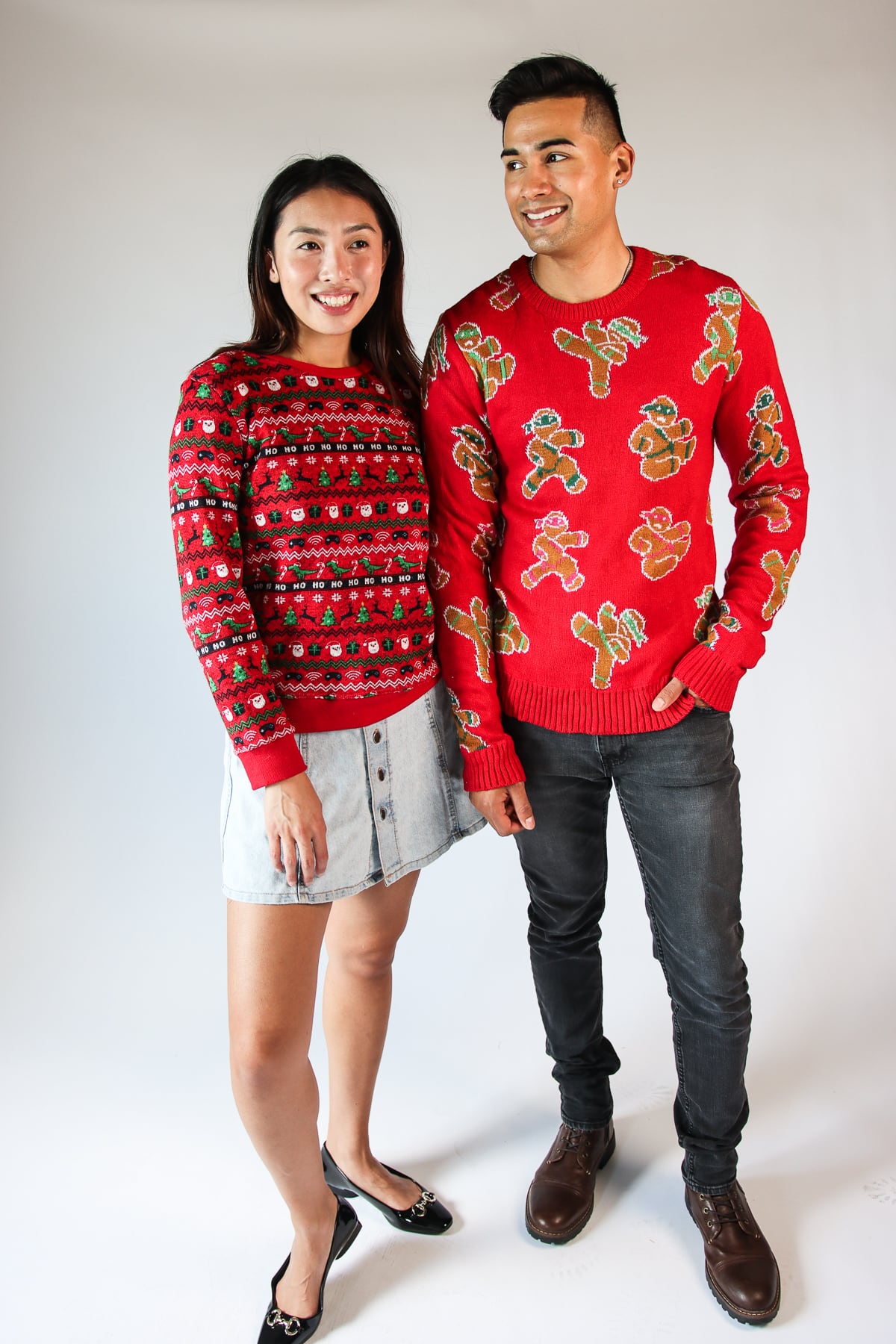 Man and woman smiling wearing red modern recycled ugly Christmas sweaters with festive patterns on white background