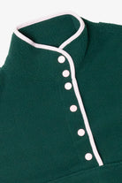 Close-up of a dark green fleece pullover with pink snap buttons and matching collar trim