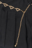 Gold chain belt with textured heart links on a black pleated skirt