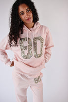 Person wearing a pink hoodie and pants with sequin numbers on a plain background
