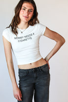 Woman wearing a white short-sleeve crop top with MOMMY NEEDS A CIGARETTE