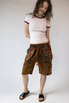 Woman wearing a white t-shirt with red trim and patterned brown shorts on a white background