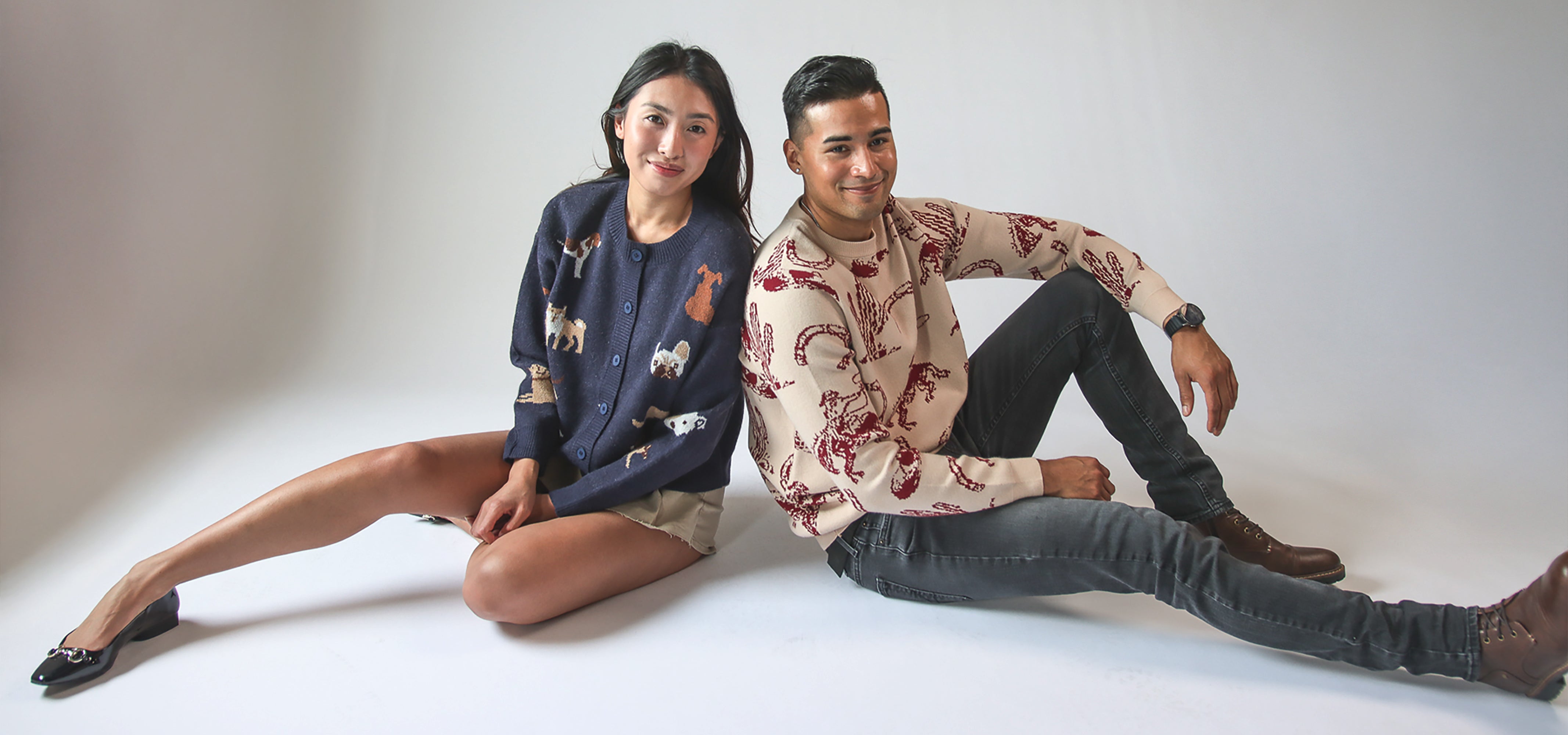 male and female model sitting together wearing graphic sweaters