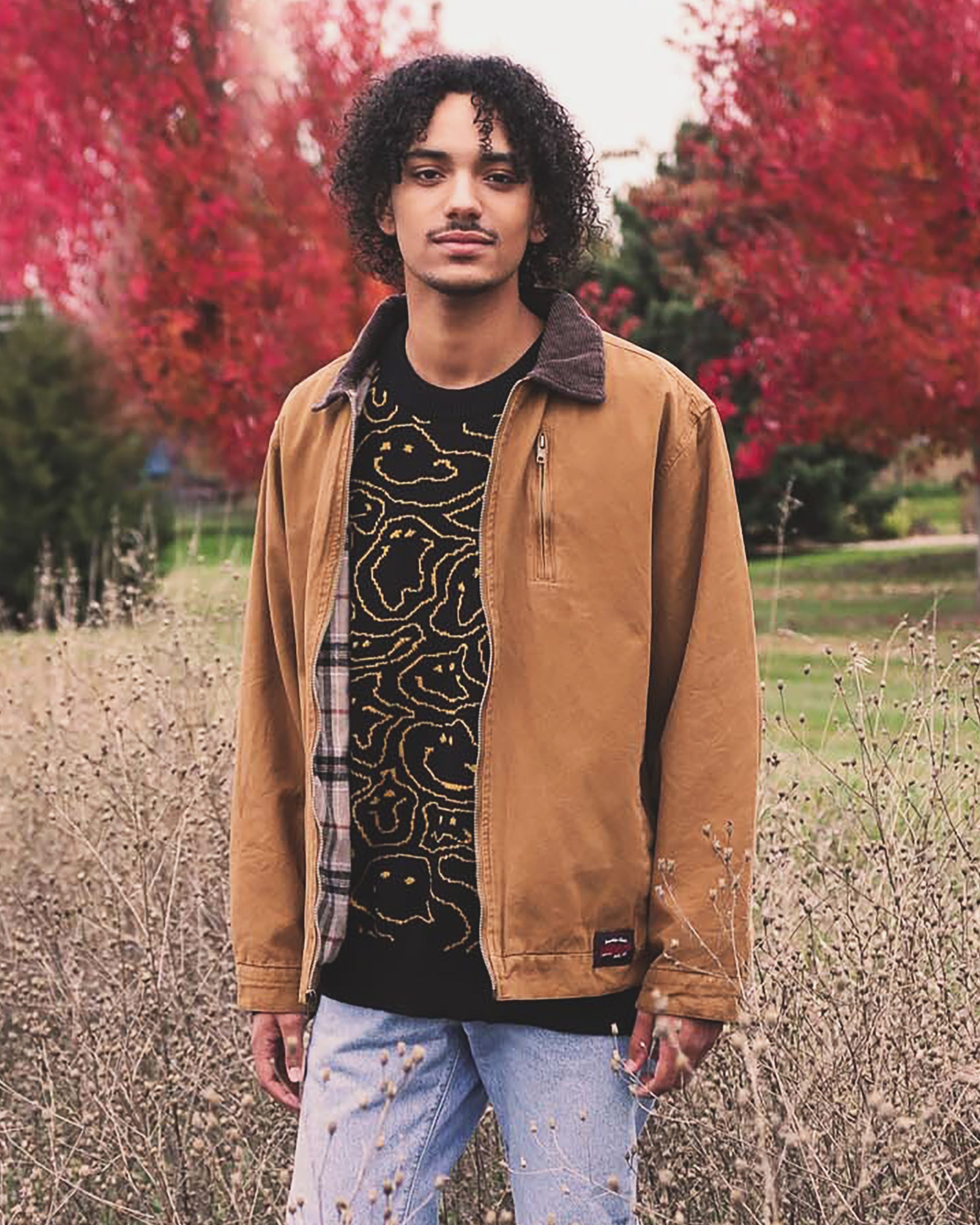 male model wearing canvas chore coat and smiley face graphic sweater