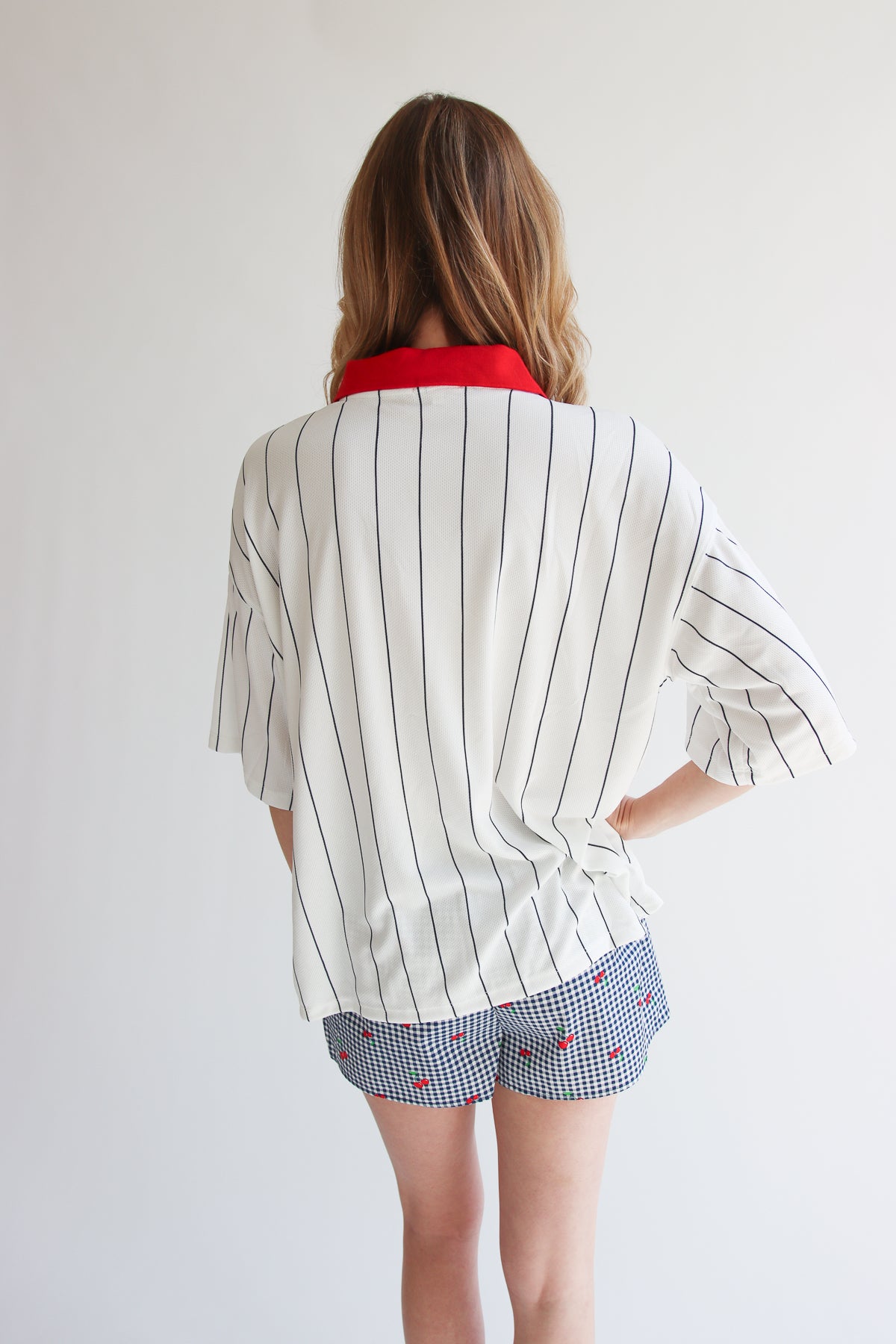 Woman wearing oversized white collared jersey with black vertical stripes and red collar, paired with patterned shorts.