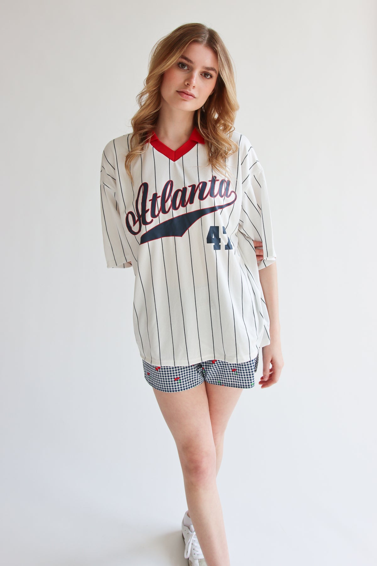 Woman wearing oversized collared jersey with Atlanta script and number 43 standing against white background