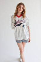 Woman wearing oversized collared jersey with Atlanta script and number 43 standing against white background