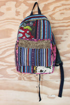 A multicolor patchwork backpack with vertical stripes, floral prints, and a brown embroidered front pocket, hanging against a light wood background.