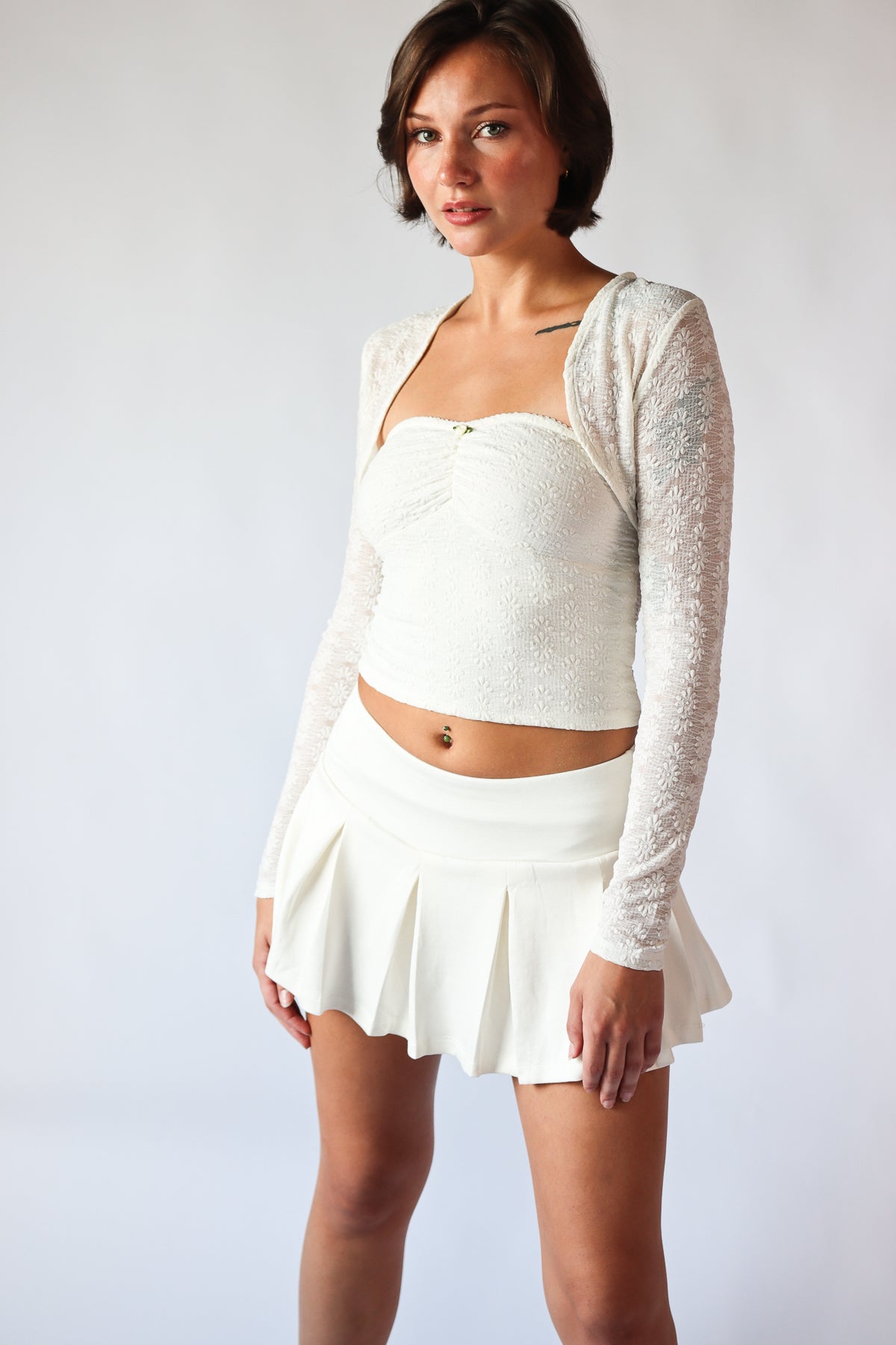 Woman wearing white pleated mini skort with elastic waistband and white textured long sleeve crop top