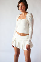 Woman wearing white pleated mini skort with elastic waistband and white textured long sleeve crop top