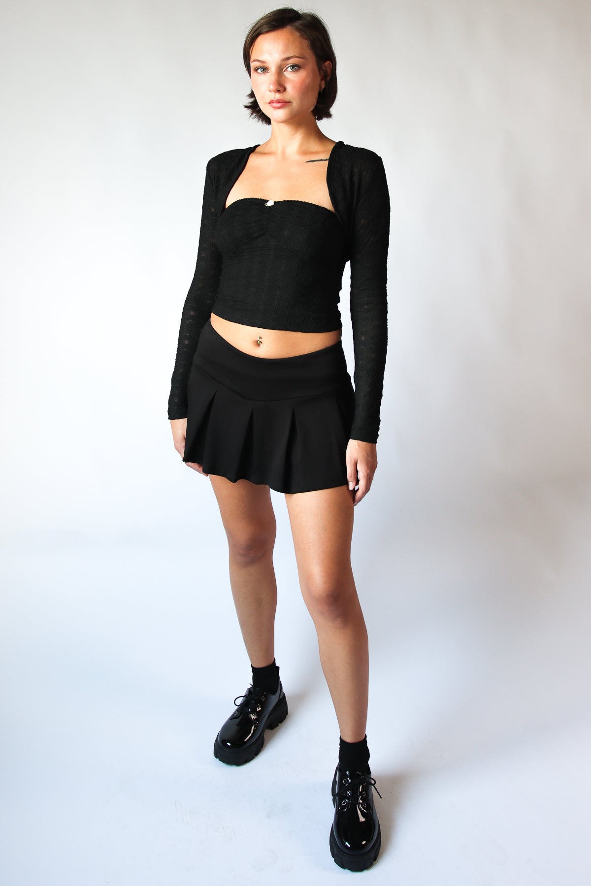 Woman wearing a black pleated mini skort with an elastic waistband and black long-sleeve cropped top and shoes