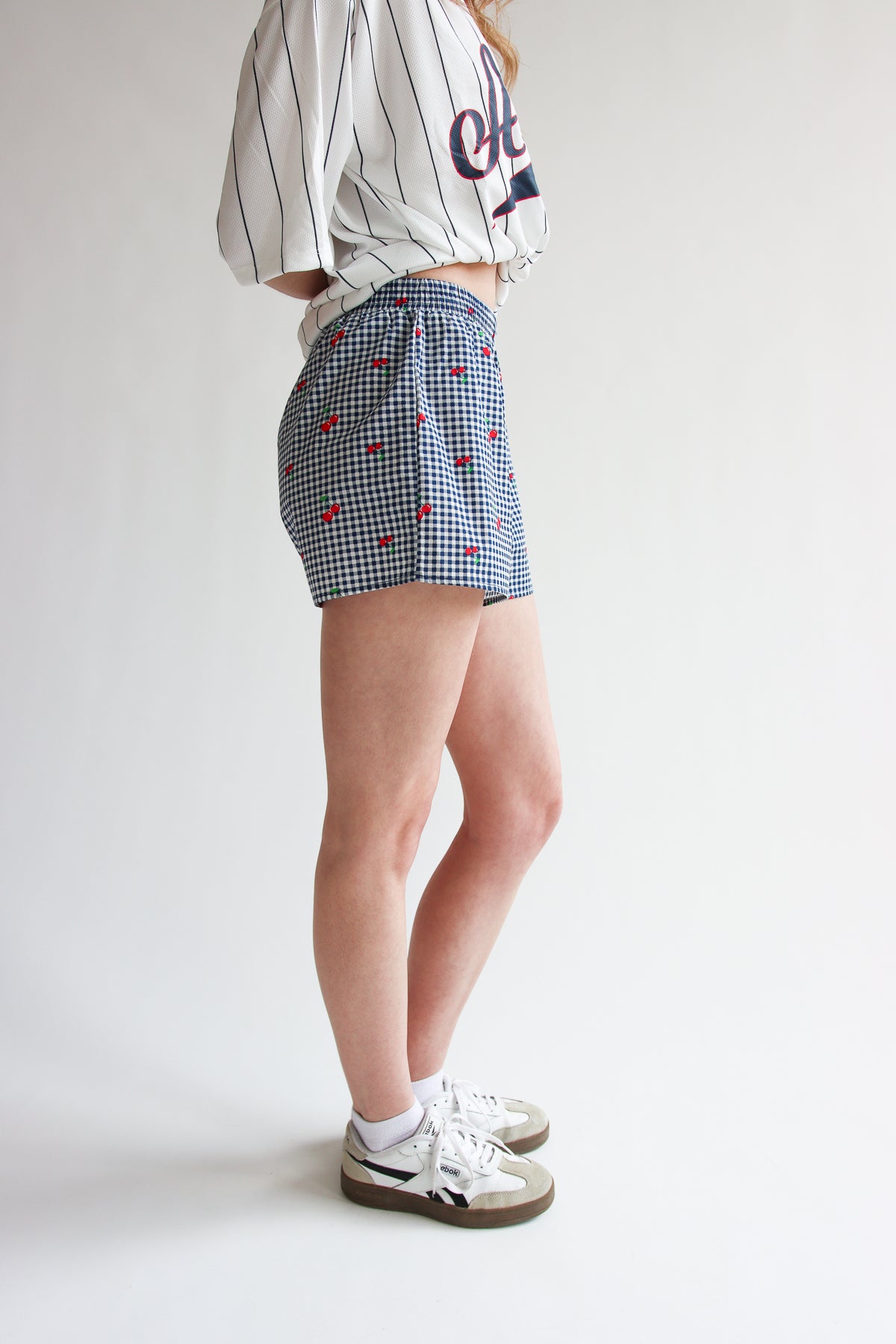 Woman wearing blue printed gingham boxer shorts with elastic waistband and white sneakers on white background