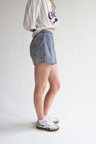 Woman wearing blue printed gingham boxer shorts with elastic waistband and white sneakers on white background