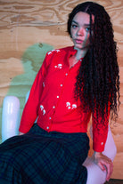 Woman wearing vintage red hand embroidered sweater with white mushroom designs sitting on white chair