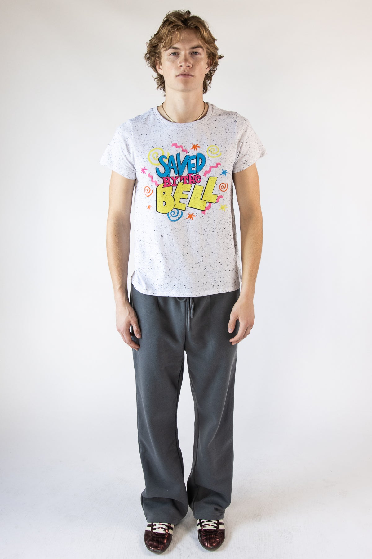 Model wearing a speckled white Saved by the Bell graphic t-shirt and charcoal grey sweatpants