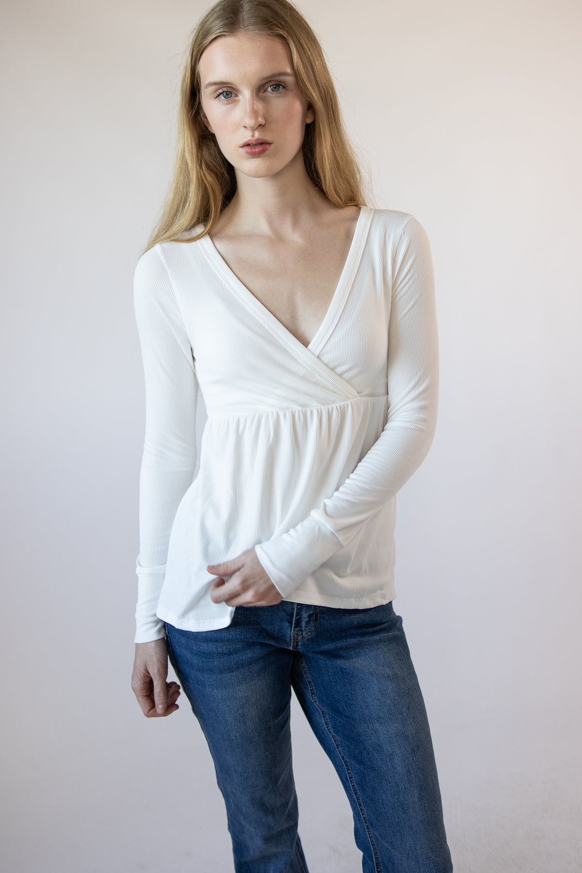 Woman wearing a white ribbed long-sleeve surplice babydoll top and blue jeans
