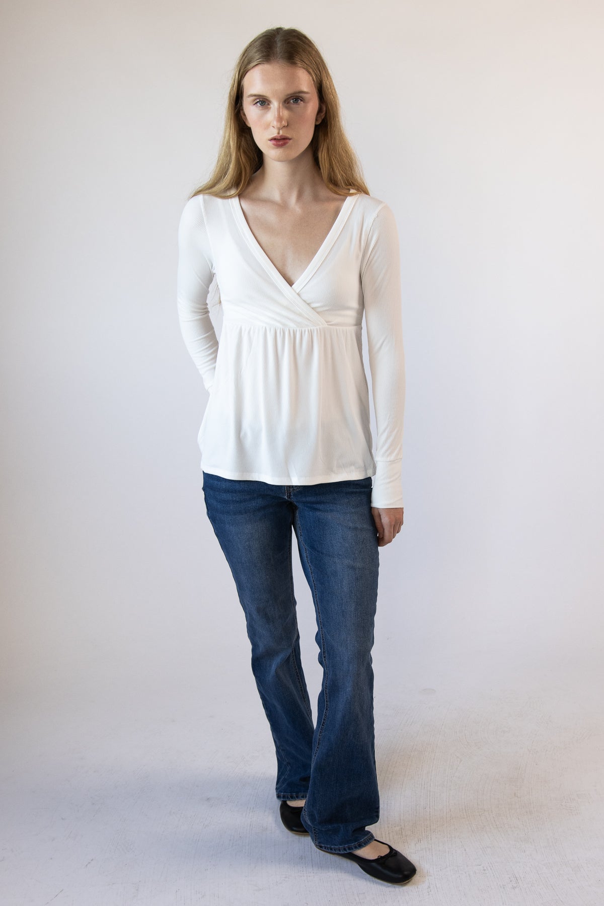 Woman wearing a white long-sleeve empire-waist wrap top with blue jeans