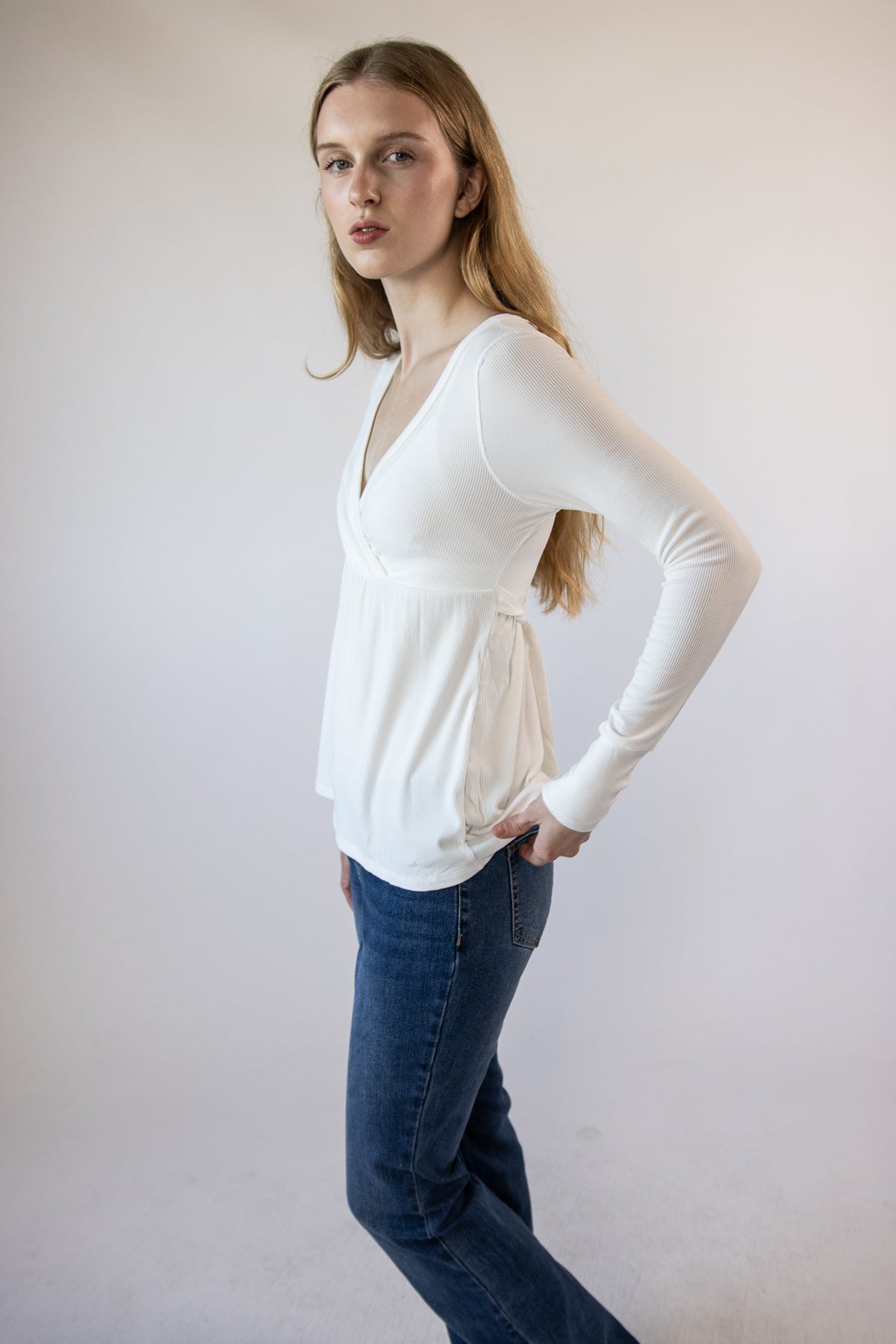 Model wearing a white ribbed crossover long-sleeve top and blue jeans